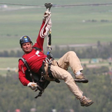 Closeup of a man ziplining with one hand.
