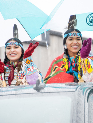 Two Native American women wave in a parade.