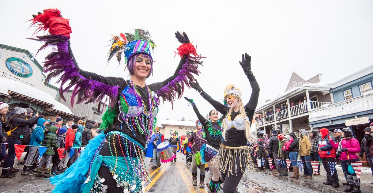 Women dressed in colorful beads and feathers dance at the Mardi Gras Parade in McCall.