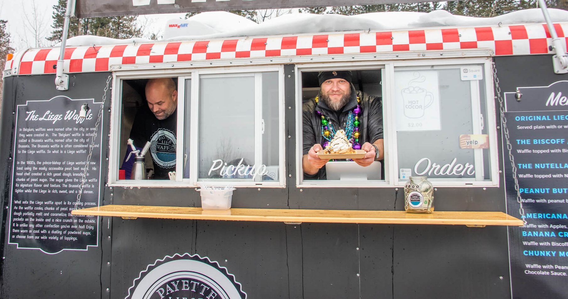 A man smiles and holds out a plate of waffles while inside a food truck.