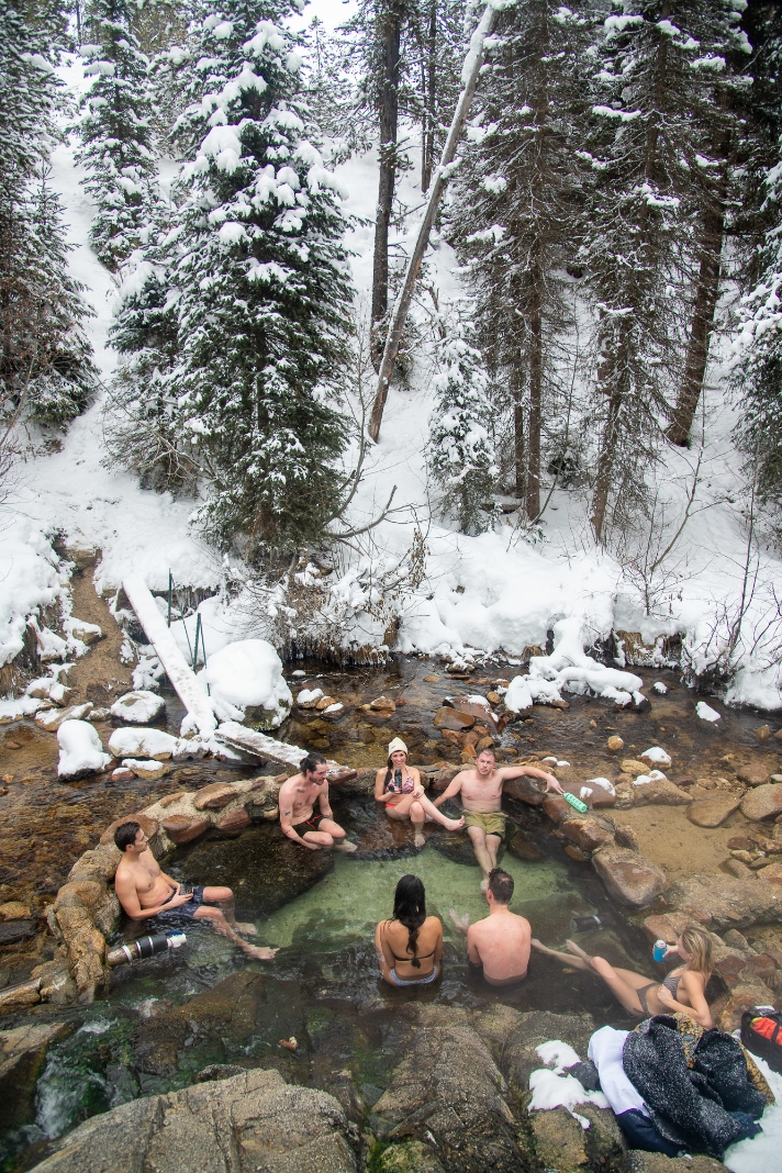 A group of people sit in a hot spring, surrounded by snow.