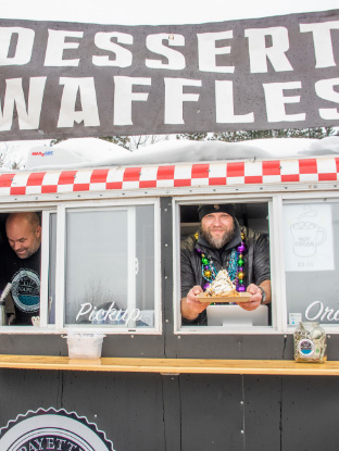 A man smiles and holds out a plate of waffles while inside a food truck.