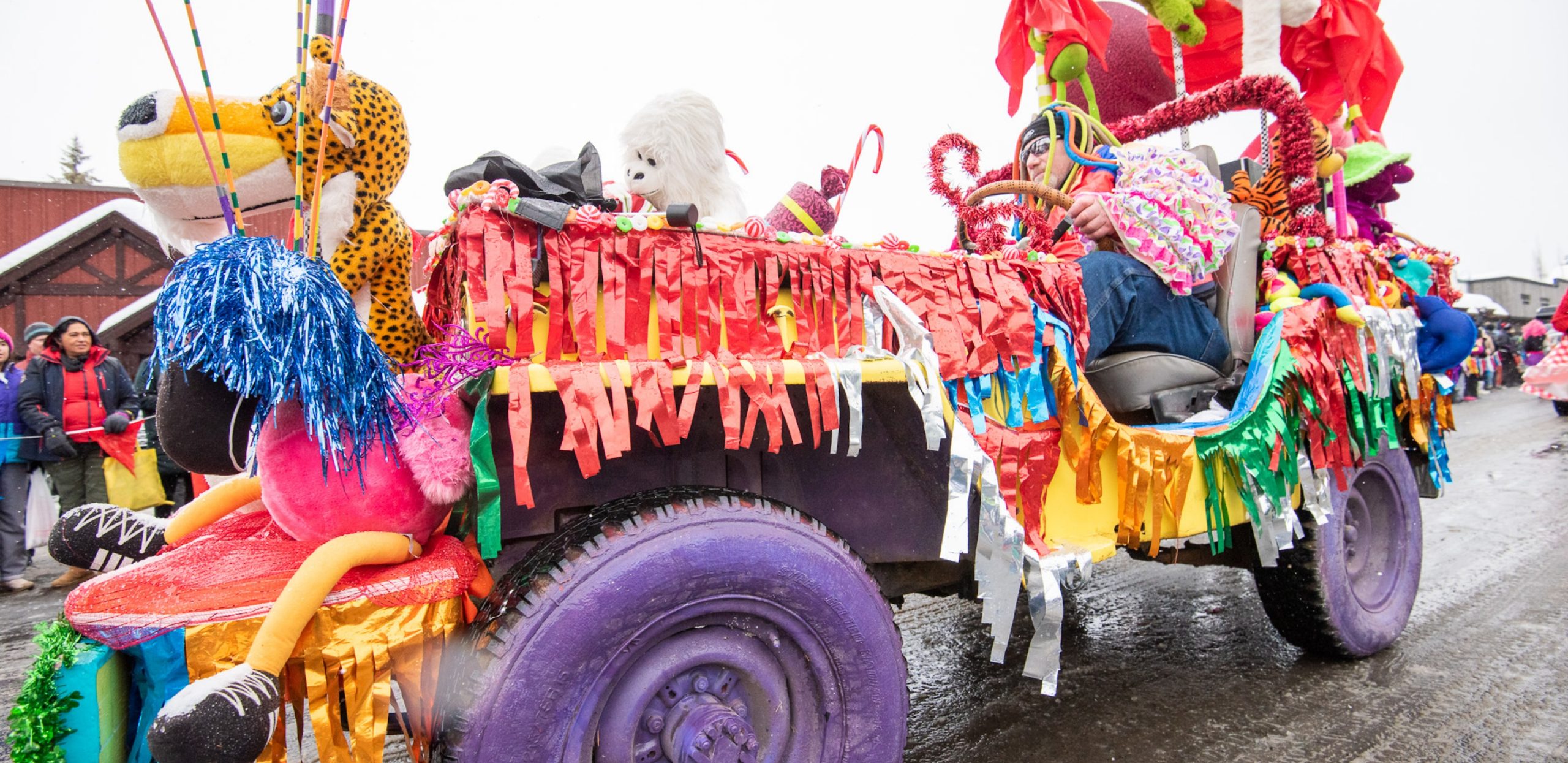 A man drives a Jeep decked out in colorful fringe, tinsel, and stuffed animals.