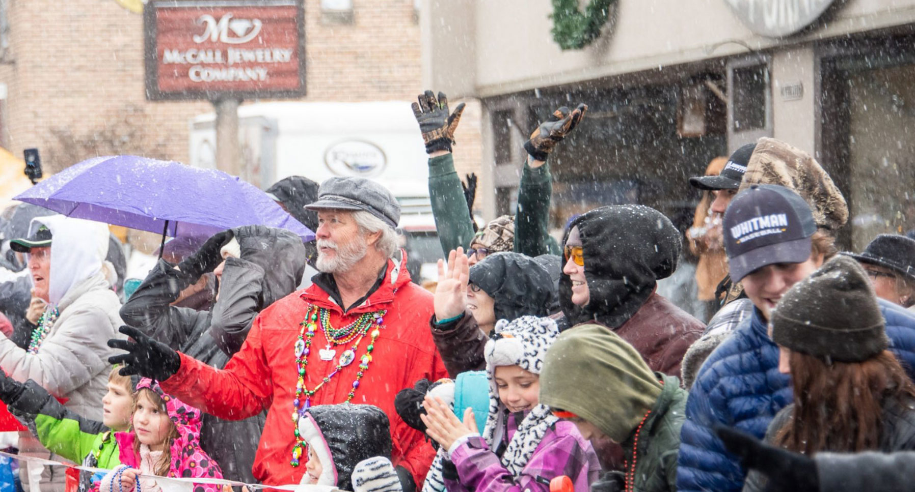 A crowd of people line a street in the snow to watch a parade.