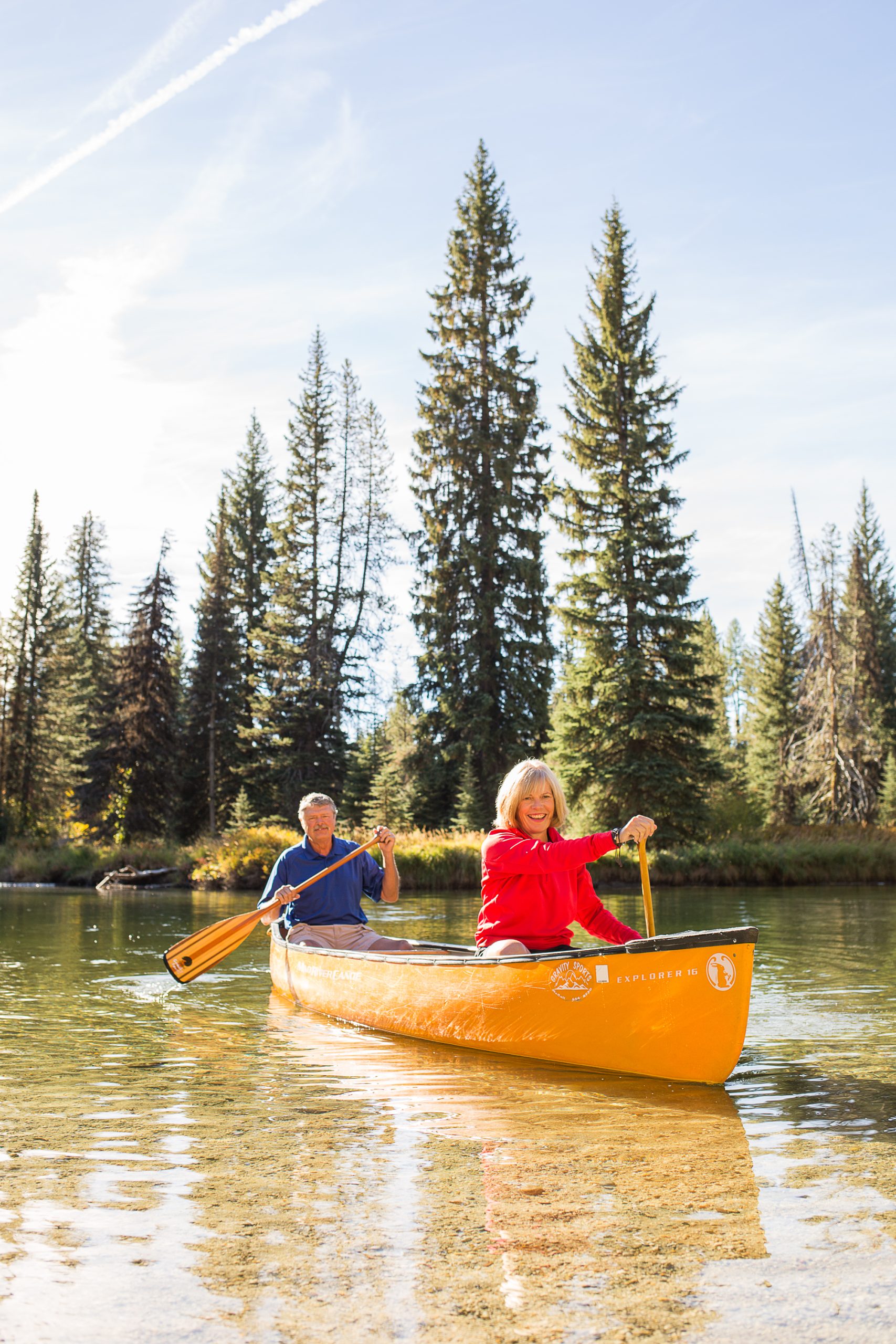 Two people paddling a canoe on the North Fork of the Payette River, surrounded by tall trees.