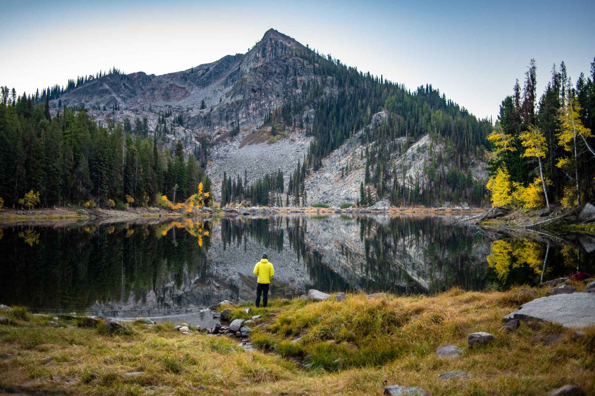 A person standing in front of Louie Lake, and in the background a mountain surrounded by forests.