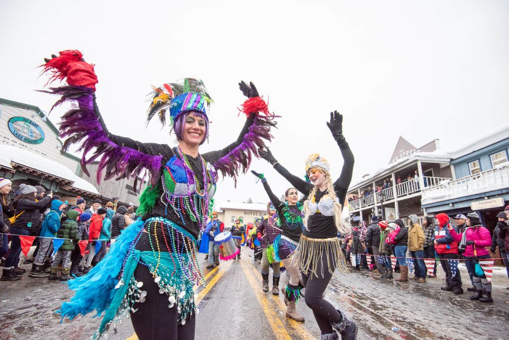 Street performers in colorful outfits dancing in the street during McCall Winter Carnival Parade.